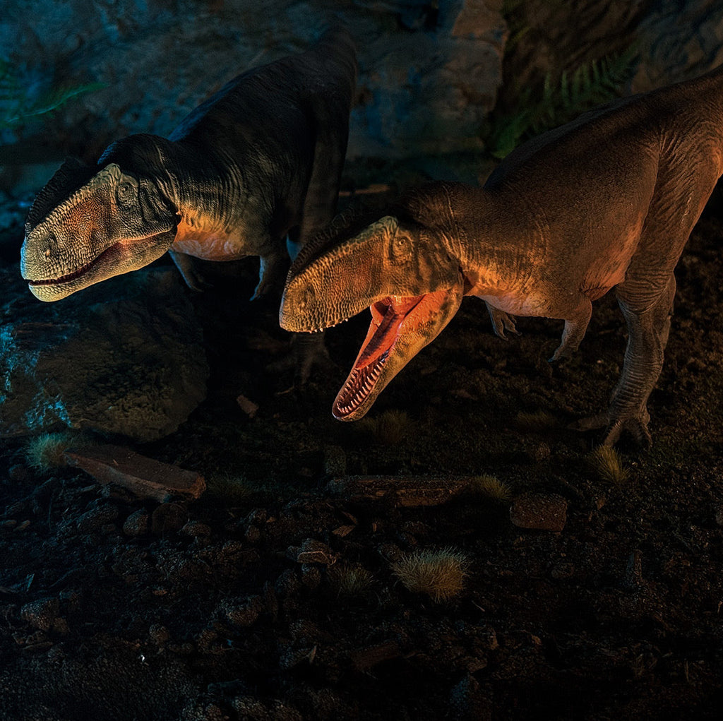 Two GIGANOTOSAURUS dinosaur models in a dark, rocky setting with glowing blue light.